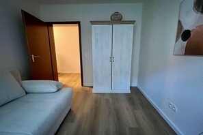 Ein Zimmer mit einem hellen Sofa, einem Kleiderschrank und einer Tür zu einem anderen Raum.