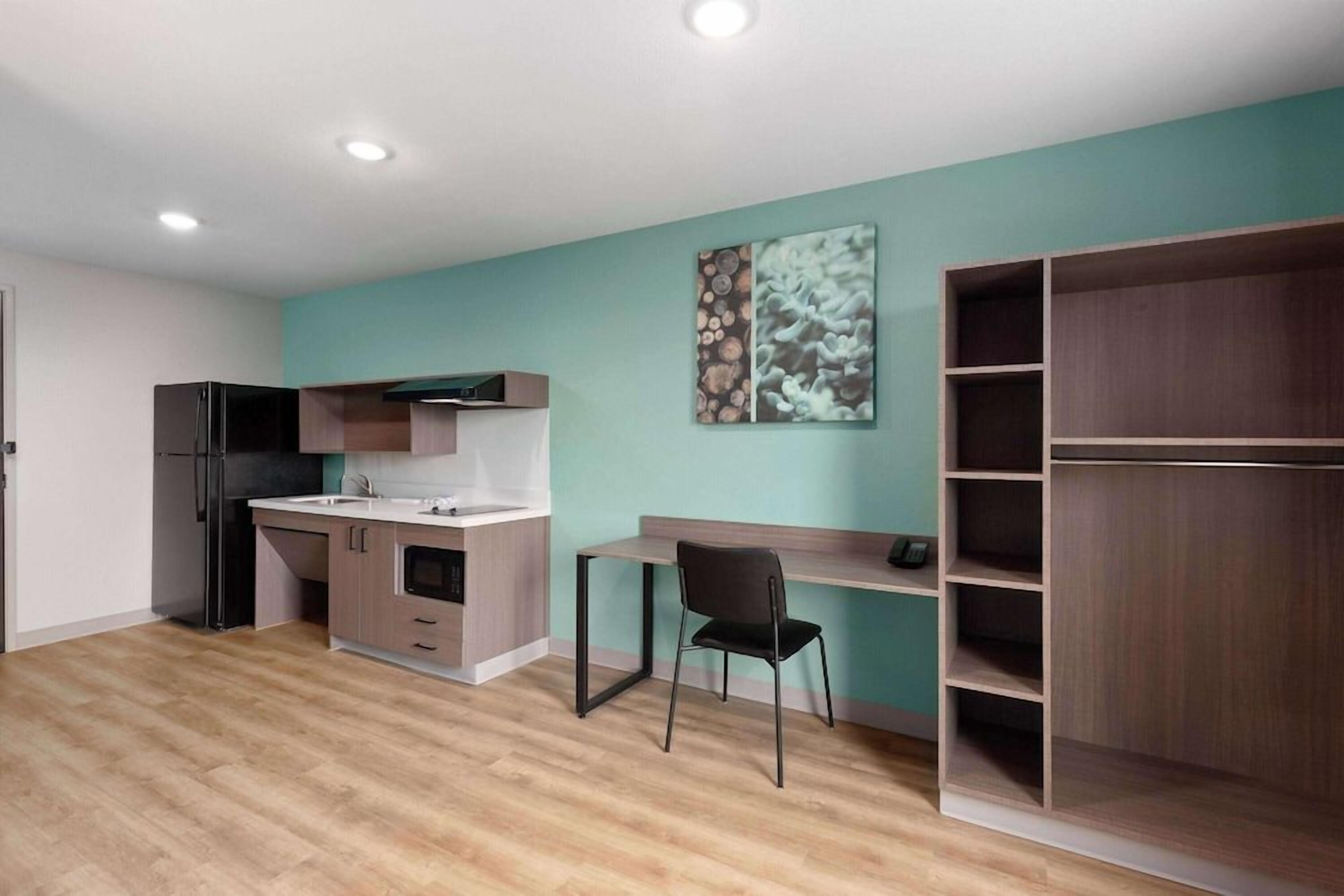 A modern kitchen with a built-in oven, a dining area with a chair, and a wooden shelving unit.