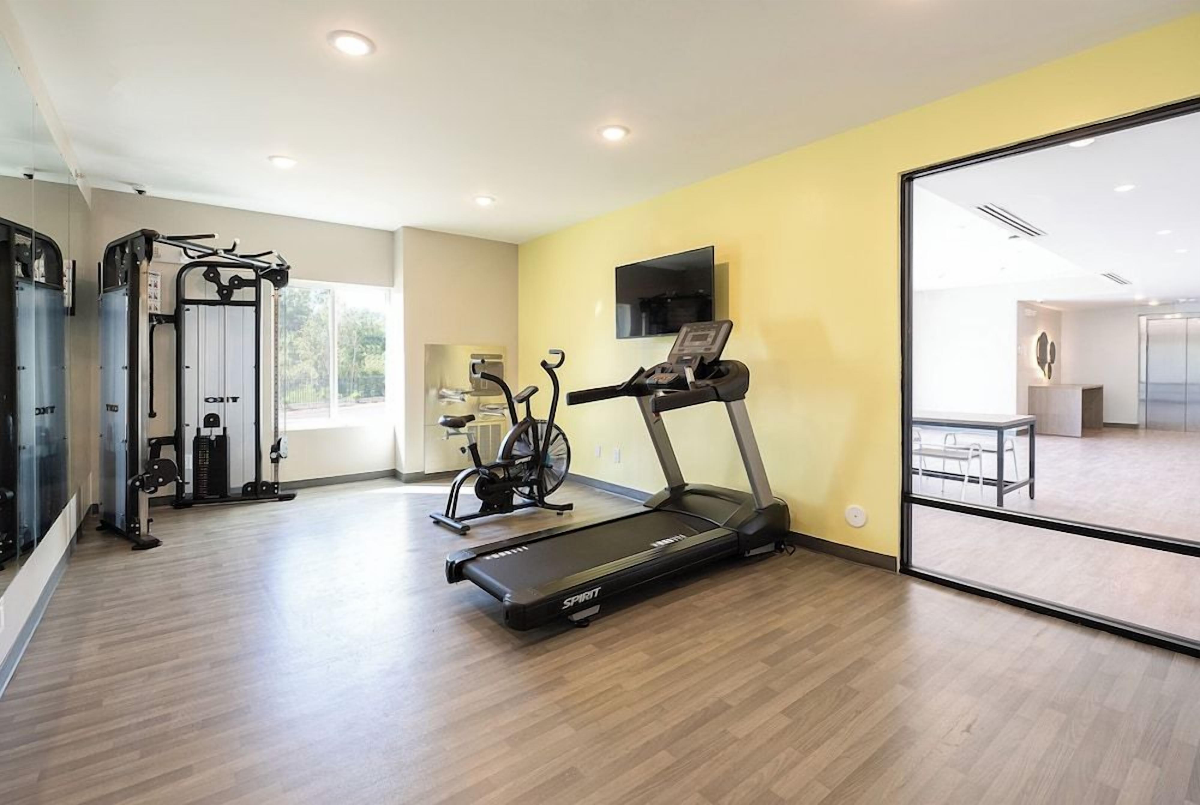 A gym with exercise equipment, a treadmill, and a TV on the wall.