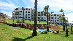 Un resort con edificios de varios pisos, una piscina y jardines ajardinados con palmeras.