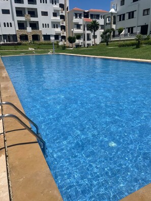 Una piscina amb aigua transparent de color blau, envoltada per un solàrium amb rajoles i una escala metàl·lica.