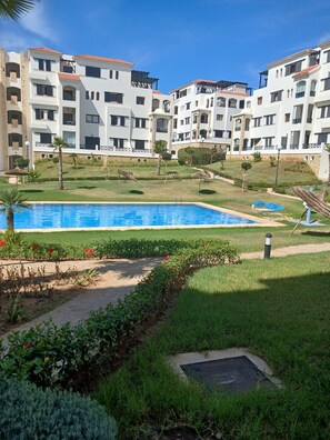 A hotel with a swimming pool, multiple balconies, and a landscaped garden. - Cosy 2-Bedroom Apartment with Pool & Garden View in Cabo Negro (Cabo Negro)