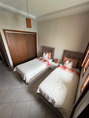 A bedroom with two beds, a wooden wardrobe, and a hanging light fixture. - Cosy 2-Bedroom Apartment with Pool & Garden View in Cabo Negro (Cabo Negro)