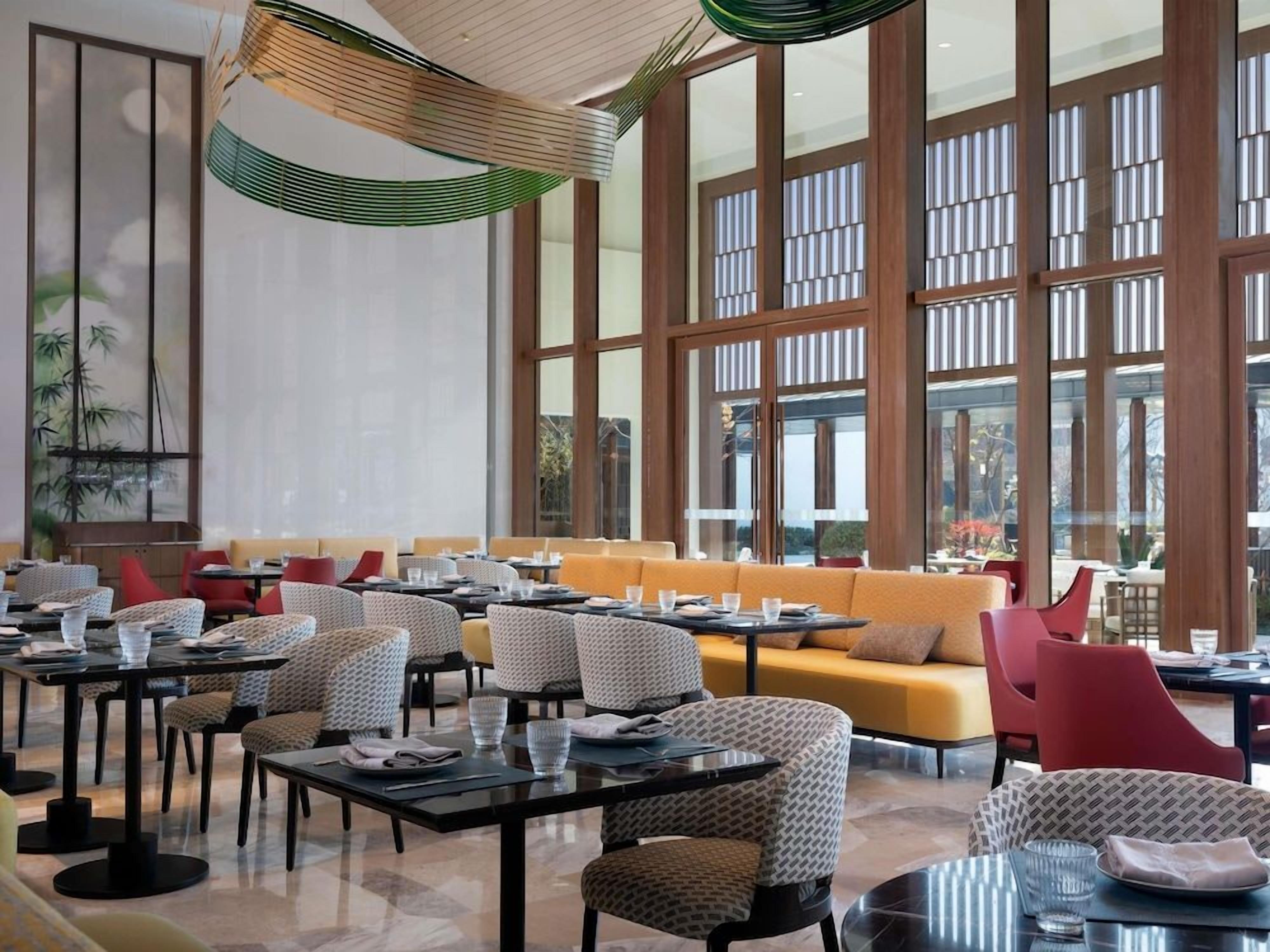 A modern dining area with high ceilings, large windows, and a variety of seating options including tables and sofas.