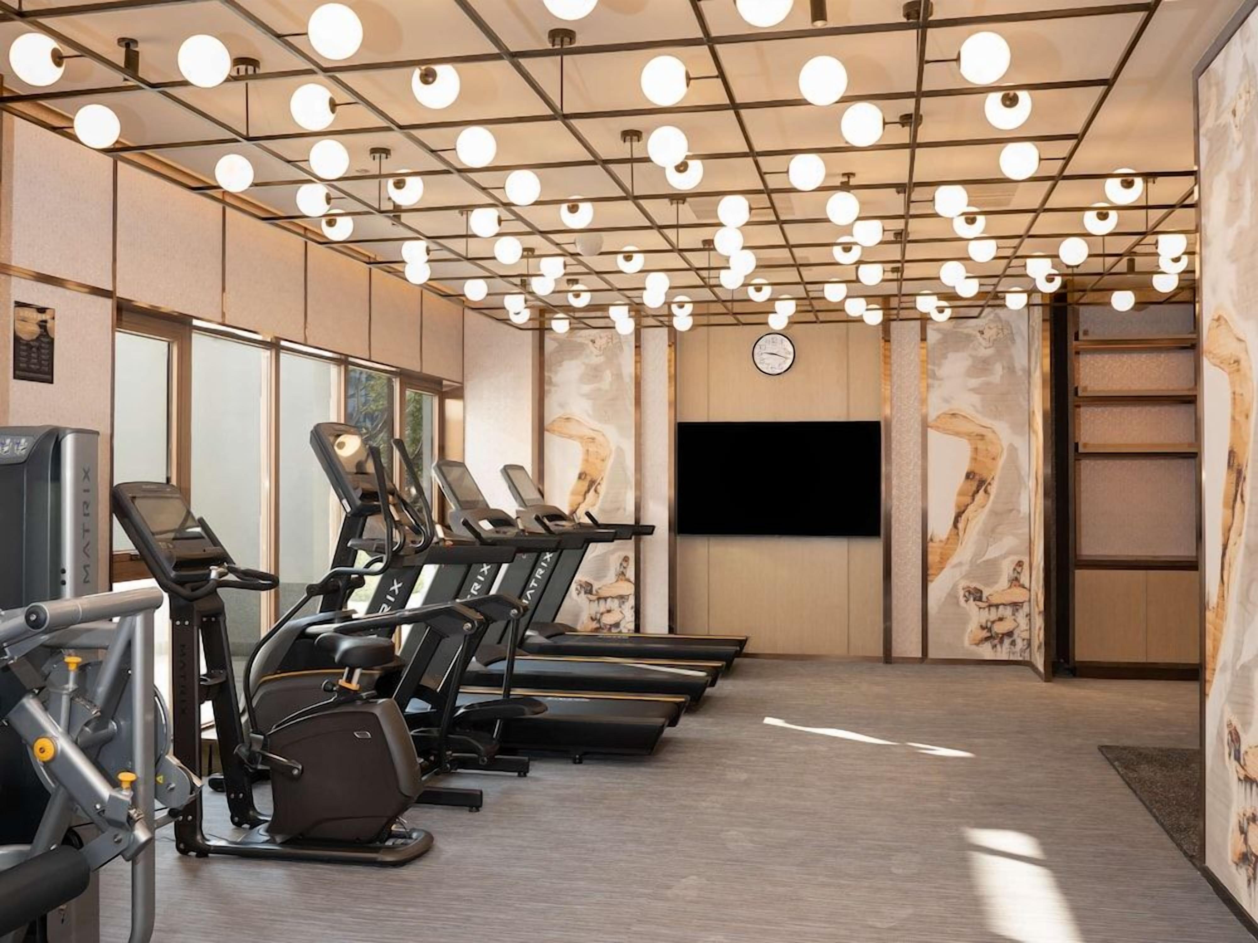 A fitness room with treadmills, a television, and a clock on the wall.