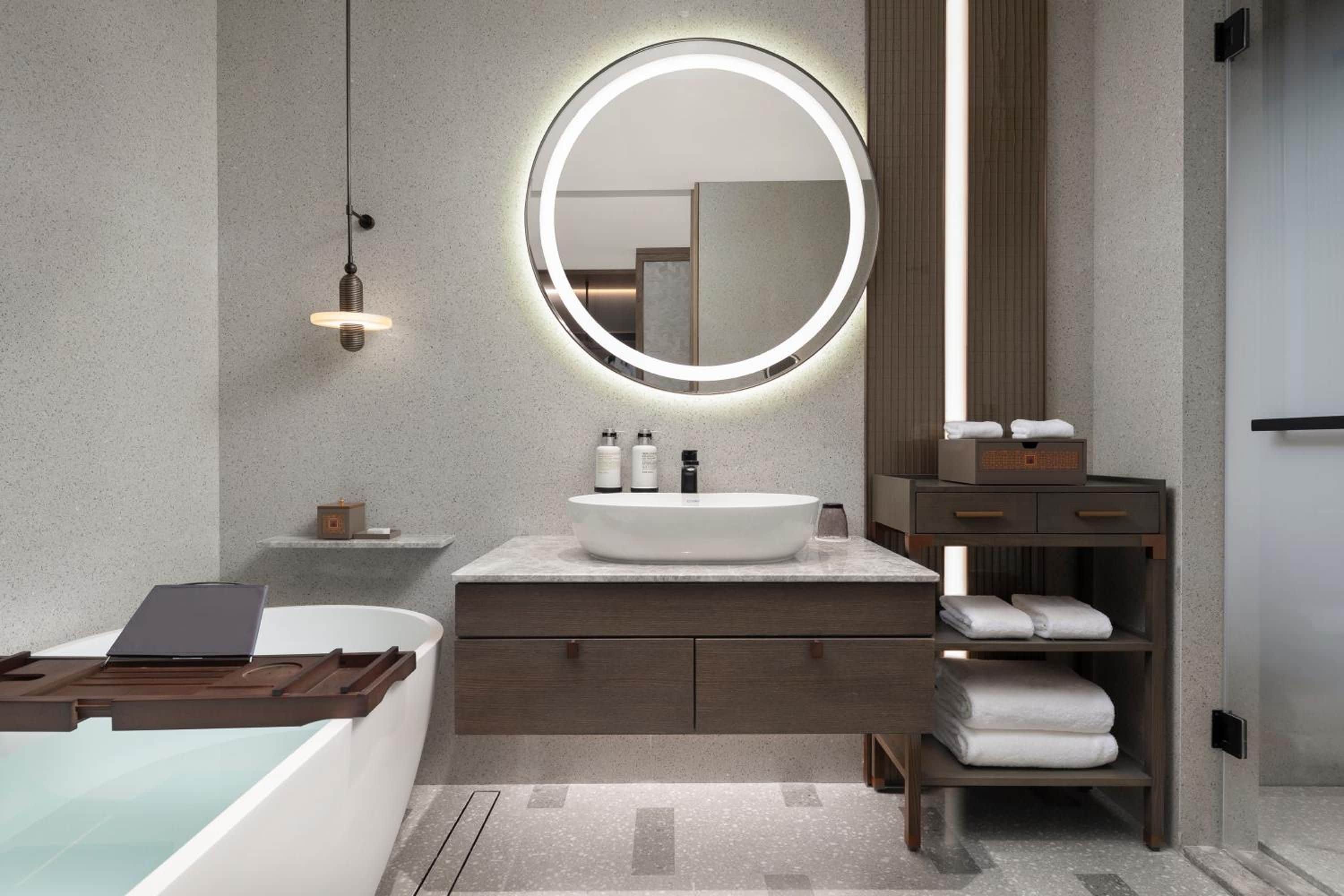 A modern bathroom with a round mirror, a bathtub, a vanity with a sink, and a towel rack.