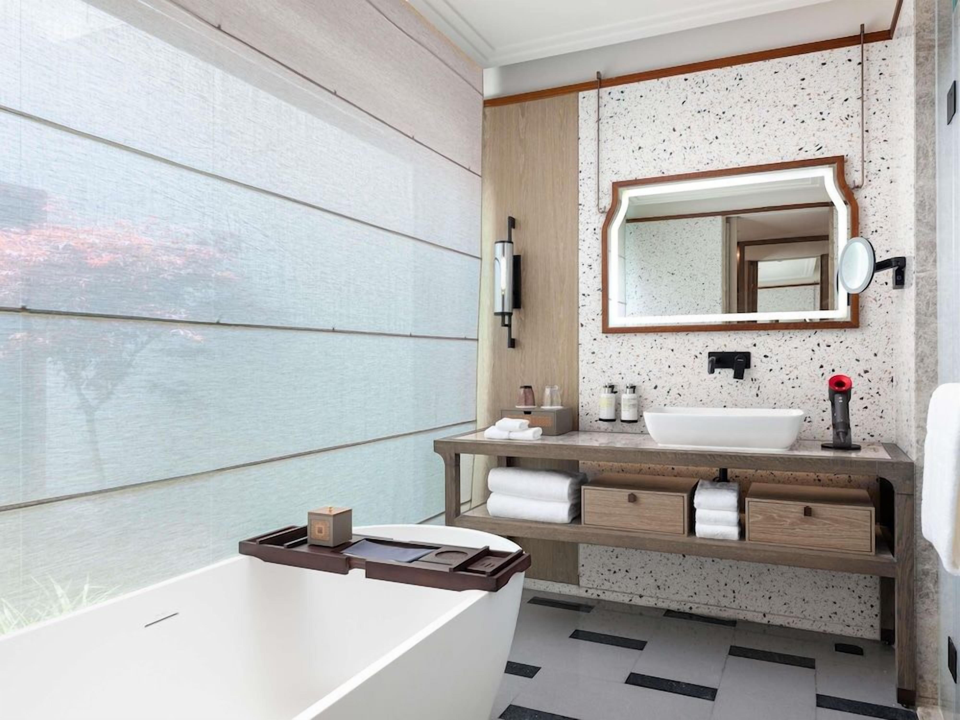 Un bagno moderno con una vasca freestanding, un mobile bagno in legno con un grande specchio e un pavimento piastrellato.