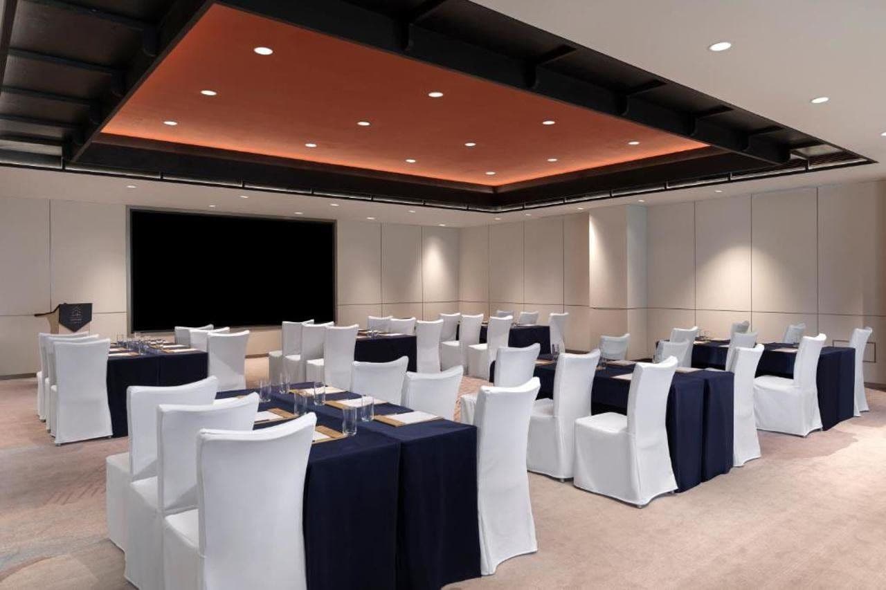 A conference room with rows of tables and chairs, a large screen, and recessed lighting.