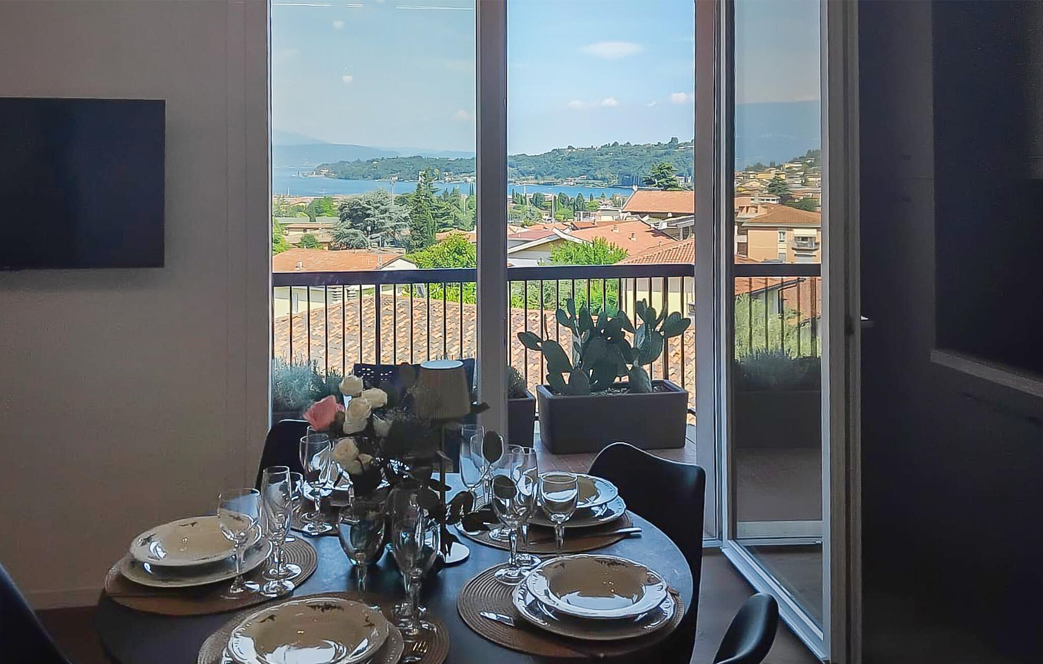 Un coin repas avec une table dressée pour quatre personnes, donnant sur un paysage côtier avec des bâtiments et un cactus.