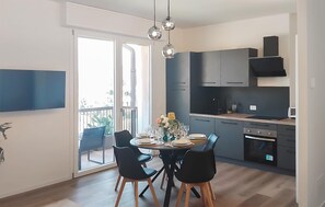 A modern kitchen with dark cabinets, a dining area with a round table and chairs, and a balcony with plants. - 1 bedroom stunning apartment in Salò (Salò)