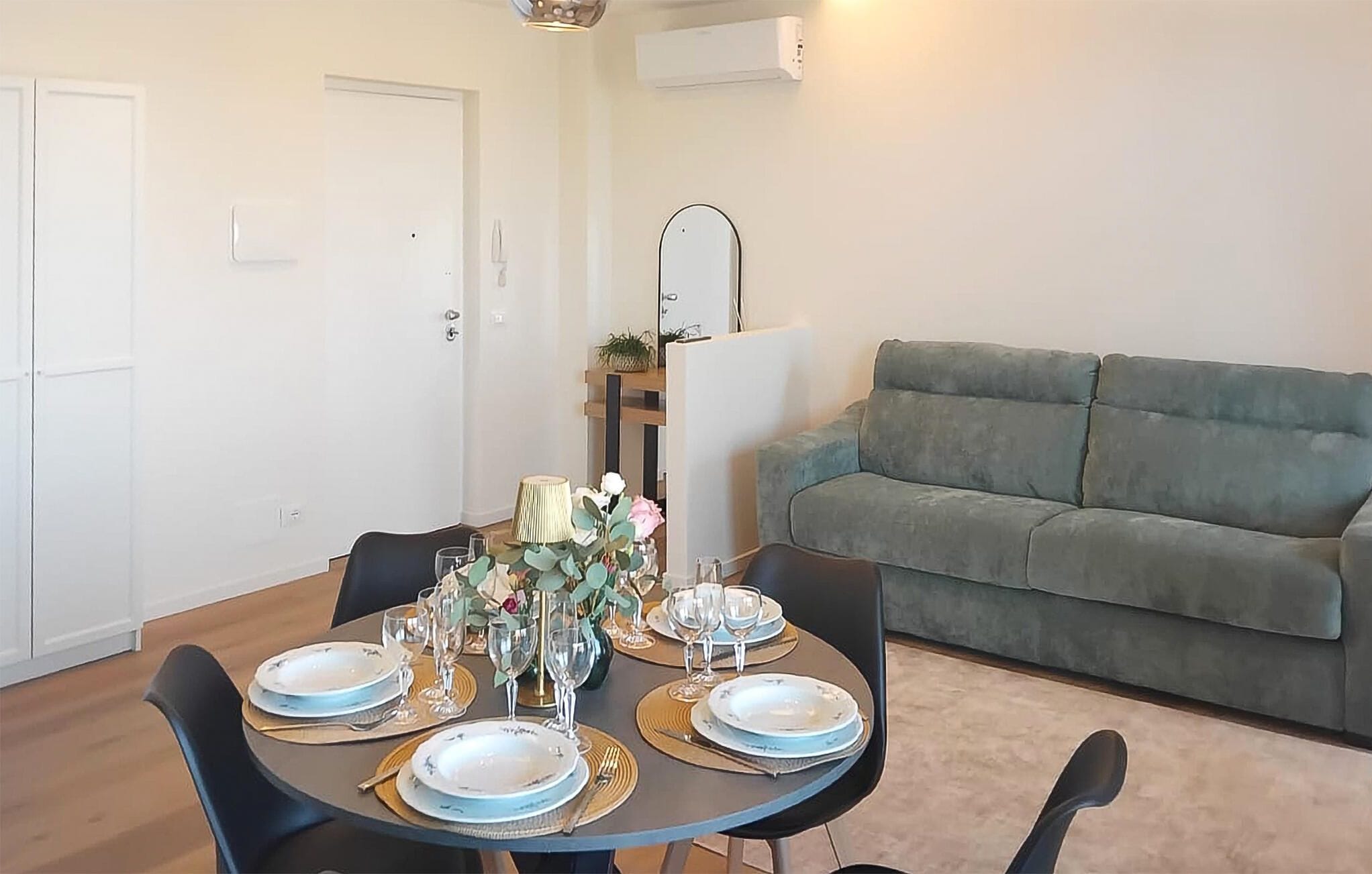 Un coin repas avec une table ronde dressée pour quatre personnes, un canapé gris et un appareil de climatisation blanc fixé au mur.
