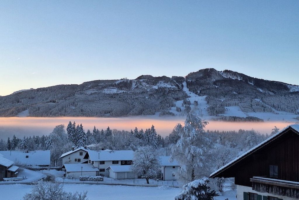 A snow-covered mountain with a ski slope, a small village with houses, and a wooden cabin.