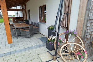 An outdoor patio with wicker furniture, a wooden table, and a decorative wagon wheel with flowers. - Pension Alpenblick Holiday Apartment Obadob (Oy-Mittelberg OT Maria-Rain)
