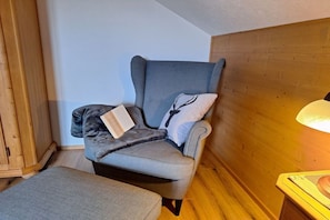 A corner room with a grey armchair, a small ottoman, and a wooden cabinet. - Pension Alpenblick Holiday Apartment Obadob (Oy-Mittelberg OT Maria-Rain)