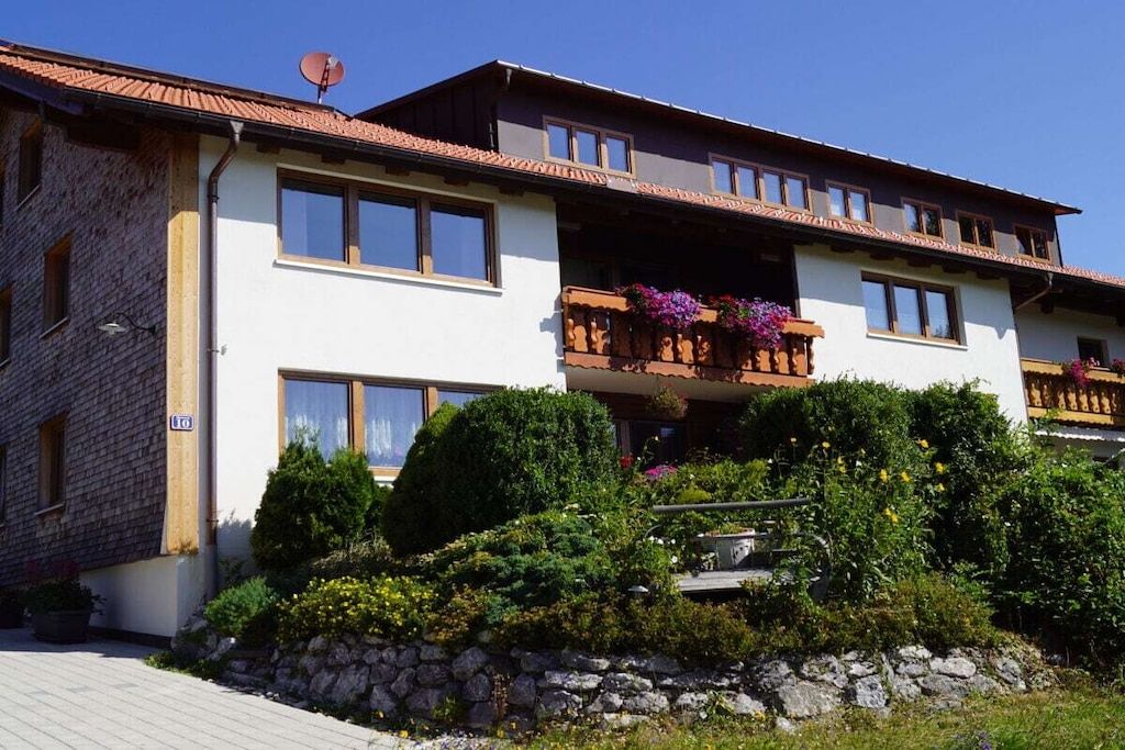 Ein zweistöckiges Gebäude mit einem Balkon, einer Steinmauer und üppiger Bepflanzung.