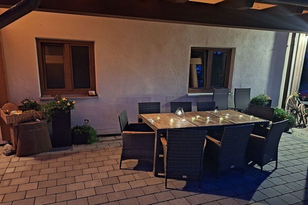 An outdoor patio with a wooden table and chairs, potted plants, and a brick floor.