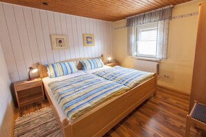 Une chambre à coucher avec un lit en bois, deux tables de chevet, une fenêtre avec des rideaux et un radiateur.