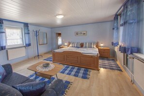 A bedroom with a wooden bed, a nightstand, a small table, a sofa, and a window with curtains. - Holiday apartment with 3 bedrooms (Impflingen)