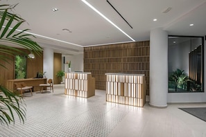 Uma área de recepção moderna com um balcão de madeira, duas áreas de estar e uma parede grande com ripas verticais.