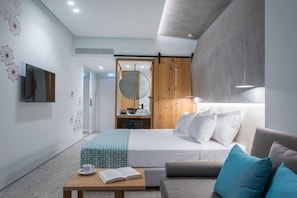 Quarto de hotel moderno com uma cama, um sofá, uma mesa de cabeceira com um livro e uma xícara, um espelho e um guarda-roupa de madeira.
