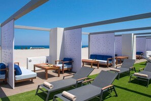 Un área de lounge en la azotea con disposición de asientos, una mesa y vista al mar.
