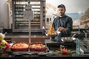 Uno chef prepara cibo in cucina con vista sul paesaggio costiero.
