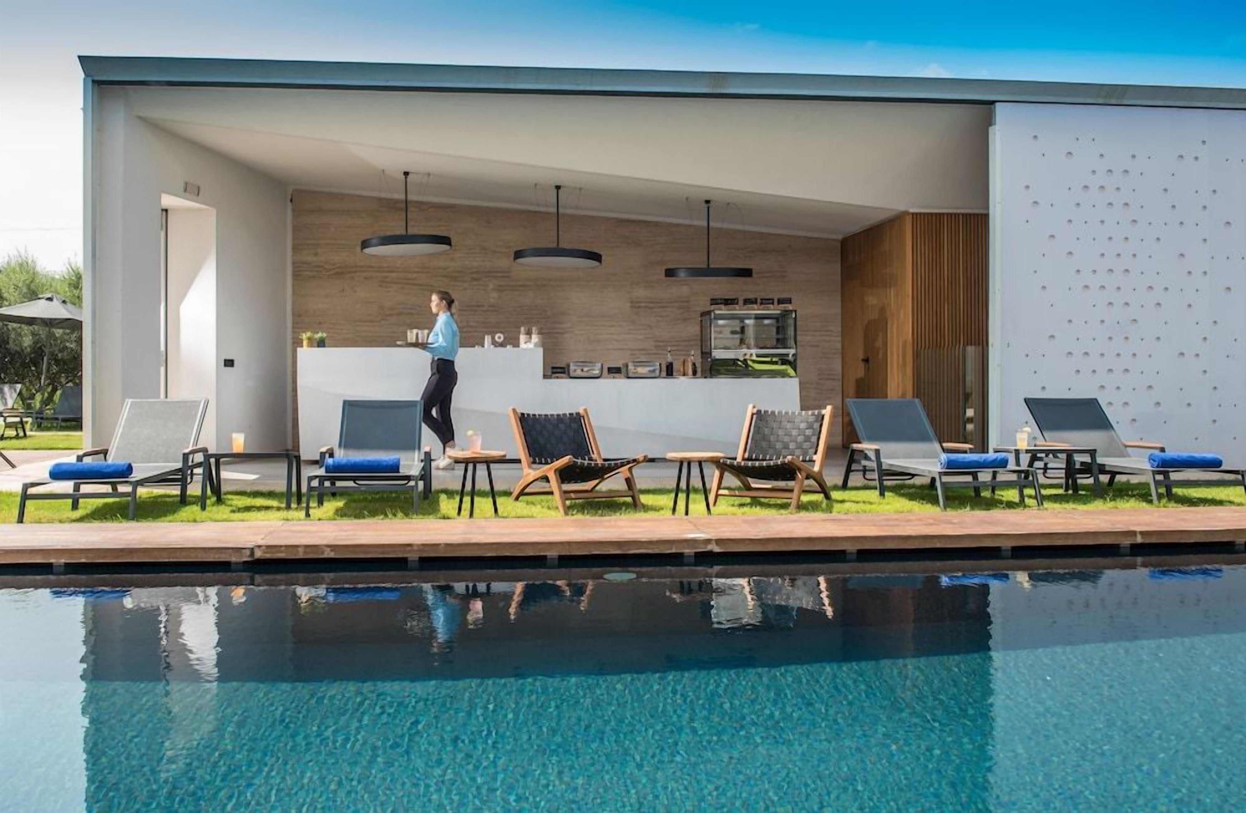 A modern outdoor pool area with lounge chairs, a bar area, and a person walking.
