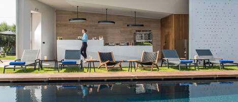 A modern outdoor pool area with lounge chairs, a bar area, and a person walking.