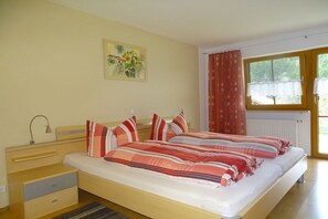 Ein Zimmer mit einem Bett, einem Nachttisch, einer Lampe und einem Fenster mit Vorhängen.