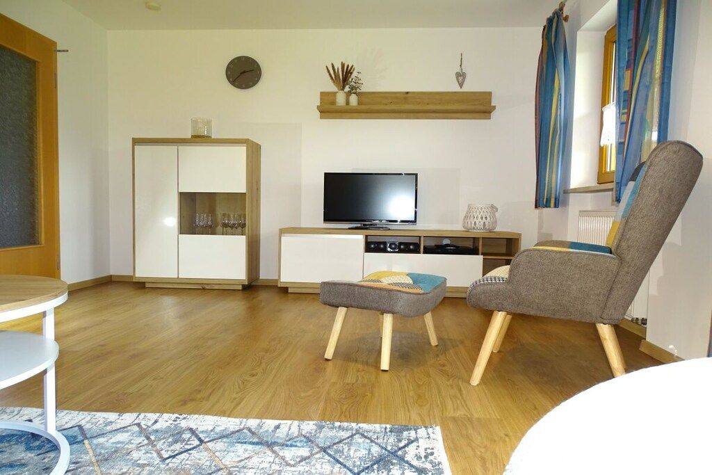 Una sala de estar con televisión, un mueble, una silla y una mesita.