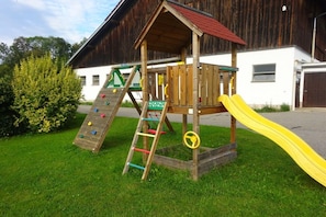 Een houten speeltoestel met een glijbaan, een klimladder en verschillende klimgrepen.