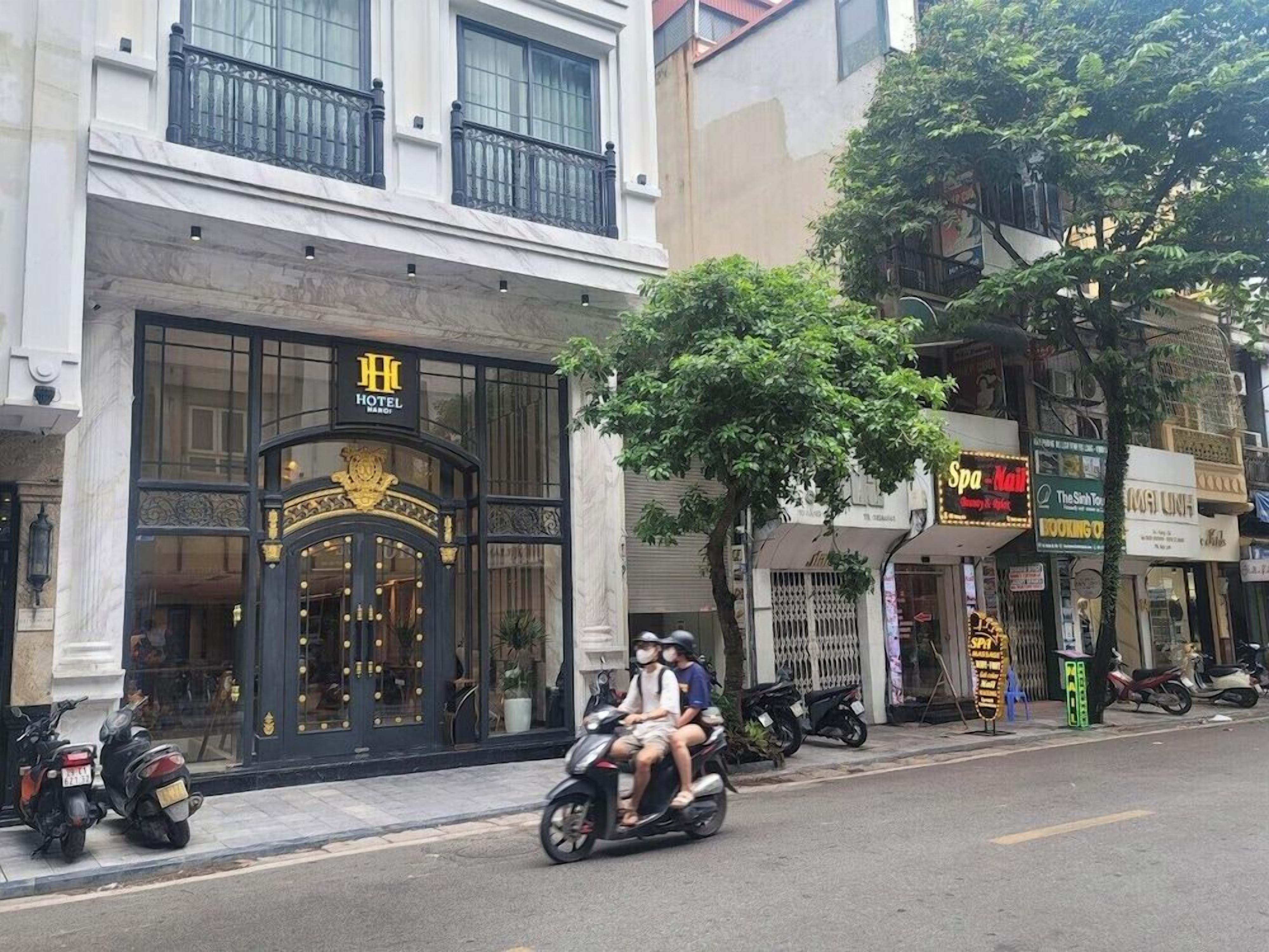 A hotel with a prominent entrance, a balcony, and a tree in front.