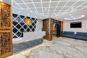 Ein Hotel-Empfangsbereich mit Marmorboden, einer Rezeption mit Firmenlogo, einer Sitzecke mit Sofas und einem modernen Deckenstil.