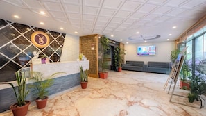 A hotel reception area with a marble floor, a reception desk, seating area, and a TV screen. - Yashshree Sikkim Blossom (Gangtok)