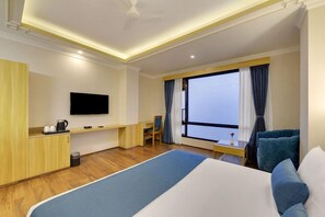 A hotel room with a bed, a desk, a television, and a large window with curtains. - Yashshree Sikkim Blossom (Gangtok)