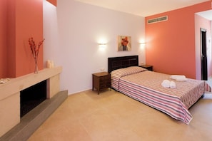 A bedroom with a bed, bedside tables, a fireplace, and a wall-mounted artwork. - Aenaon Apartments (Nafplio)