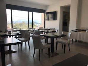 Uma área de refeições com várias mesas e cadeiras, uma televisão de tela plana na parede e vista para o exterior.