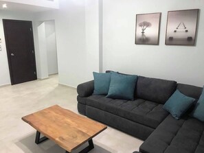 A living room with a dark grey sofa, a wooden coffee table, and two framed artworks on the wall. - Aenaon Apartments (Nafplio)