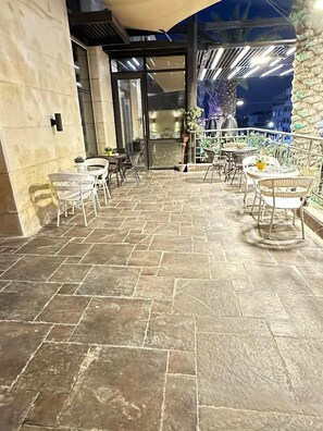 Un patio al aire libre con suelo de piedra, sillas de mimbre blanco y mesas.