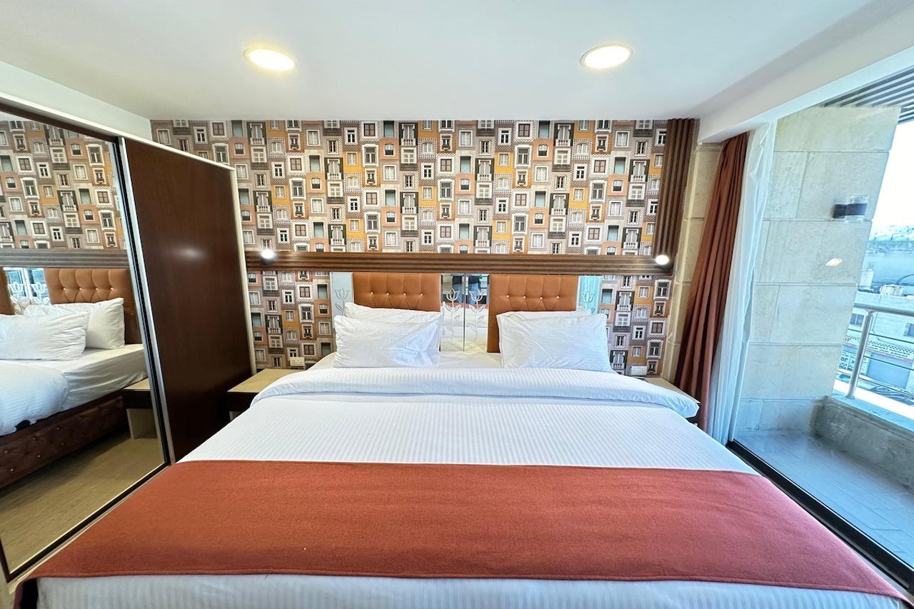 A hotel room with a large bed, a mirror, a patterned wall, and a view of the city.