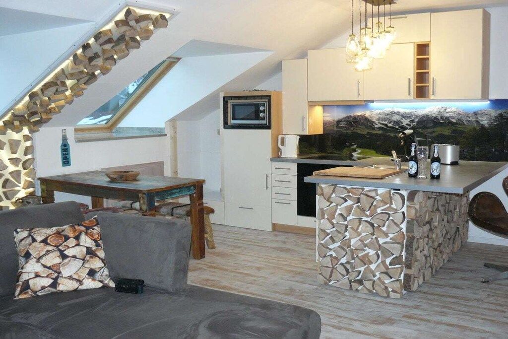 A compact kitchen with a stone island, a dining area with a table and chairs, and a view of a mountainous landscape through a window.