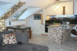 A compact kitchen with a stone island, a dining area with a table and chairs, and a view of a mountainous landscape through a window. - Holiday apartment with 2 bedrooms (Oberstdorf)