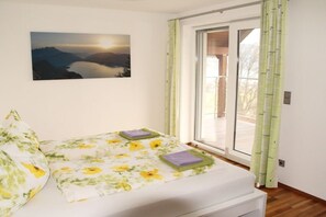Quarto com cama, janela com cortinas de bambu e pintura de uma paisagem.