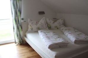 Ein Einzelbett mit blumigem Bettbezug, ein Nachttisch und ein Fenster mit Vorhängen.