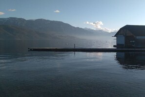 A calm lake with a wooden dock extending into the water, surrounded by mountains. - Dream house on Lake Attersee (Nußdorf)