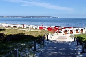 A beachside walkway leading to beach huts with a view of the sea and distant land. - Holiday apartment with 1 bedroom (Ostseebad Binz)