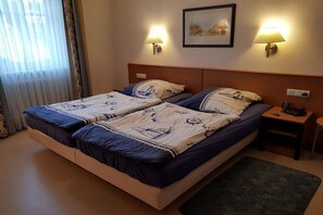 A double bed with a patterned bedspread, two bedside lamps, a framed picture on the wall, and a small bedside table with a phone and book. - Holiday apartment with 1 bedroom (Ostseebad Binz)