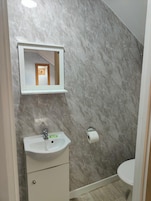 Un baño con pared de mármol, un lavabo blanco con espejo arriba y un inodoro.