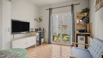 Een compacte leefruimte met een kitchenette, een flatscreen televisie, een eethoek met tafel en stoelen, en een schuifpui naar een terras.