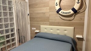 Een slaapkamer met een bed, een aan de muur bevestigd reddingsboei, een macramé gordijn en een houten vloer.